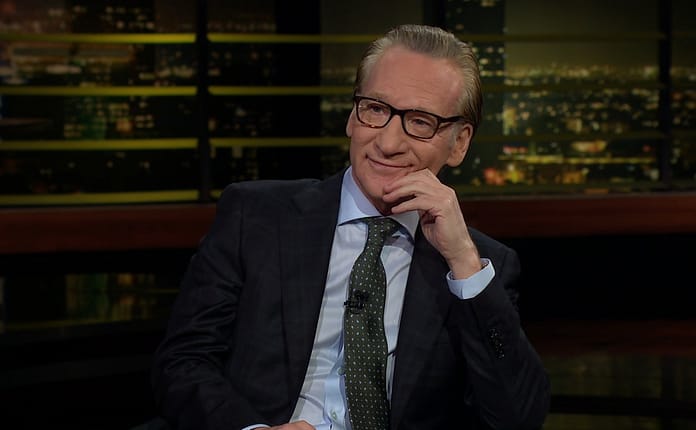 Bill Maher wearing a smug expression at his desk on set